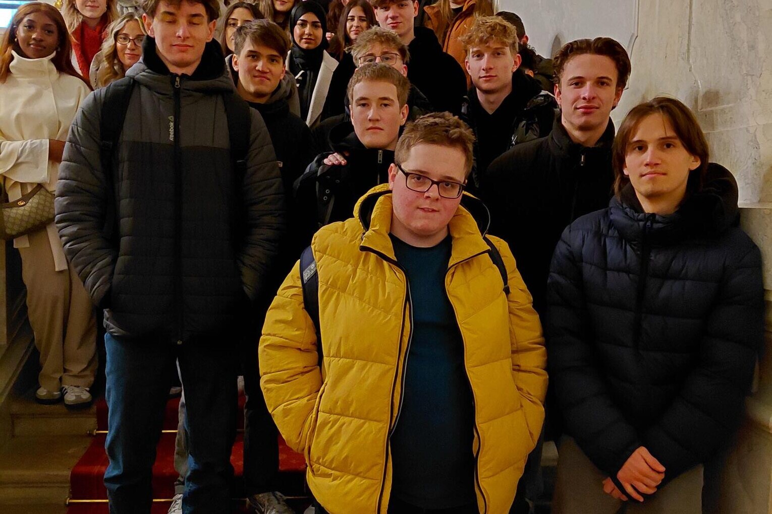 26 Schüler*innen auf Stiege stehend, direkt in die Kamera schauend.