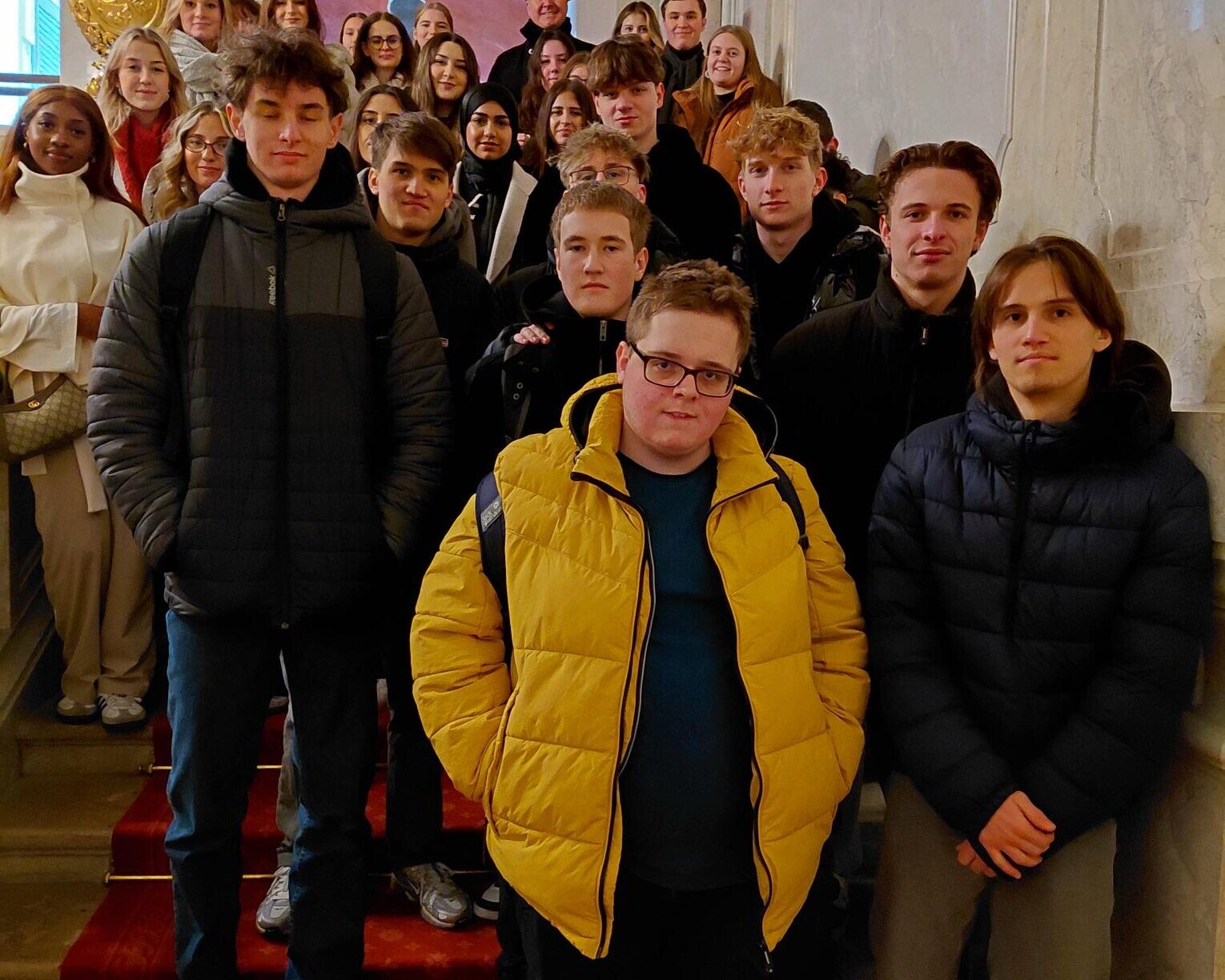 26 Schüler*innen auf Stiege stehend, direkt in die Kamera schauend.