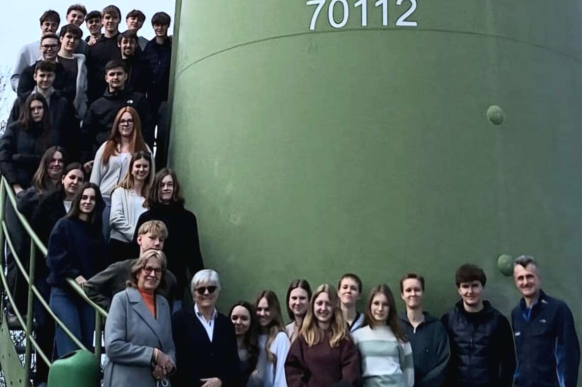Eine Gruppe von Menschen steht für ein Foto vor einem großen grünen Turm mit der Nummer „70112“, einige auf einer Treppe, andere davor auf einer Wiese.