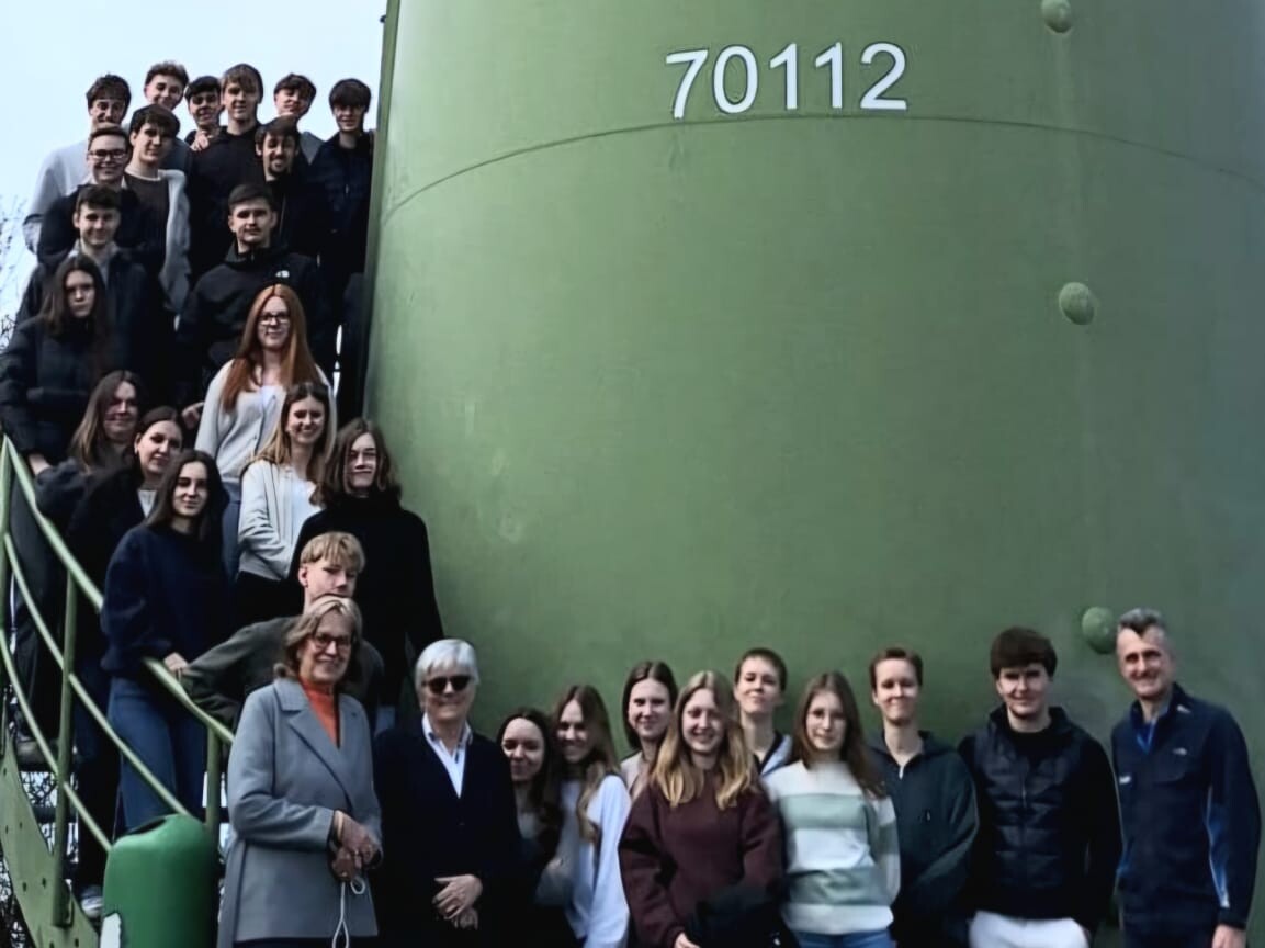 Eine Gruppe von Menschen steht für ein Foto vor einem großen grünen Turm mit der Nummer „70112“, einige auf einer Treppe, andere davor auf einer Wiese.