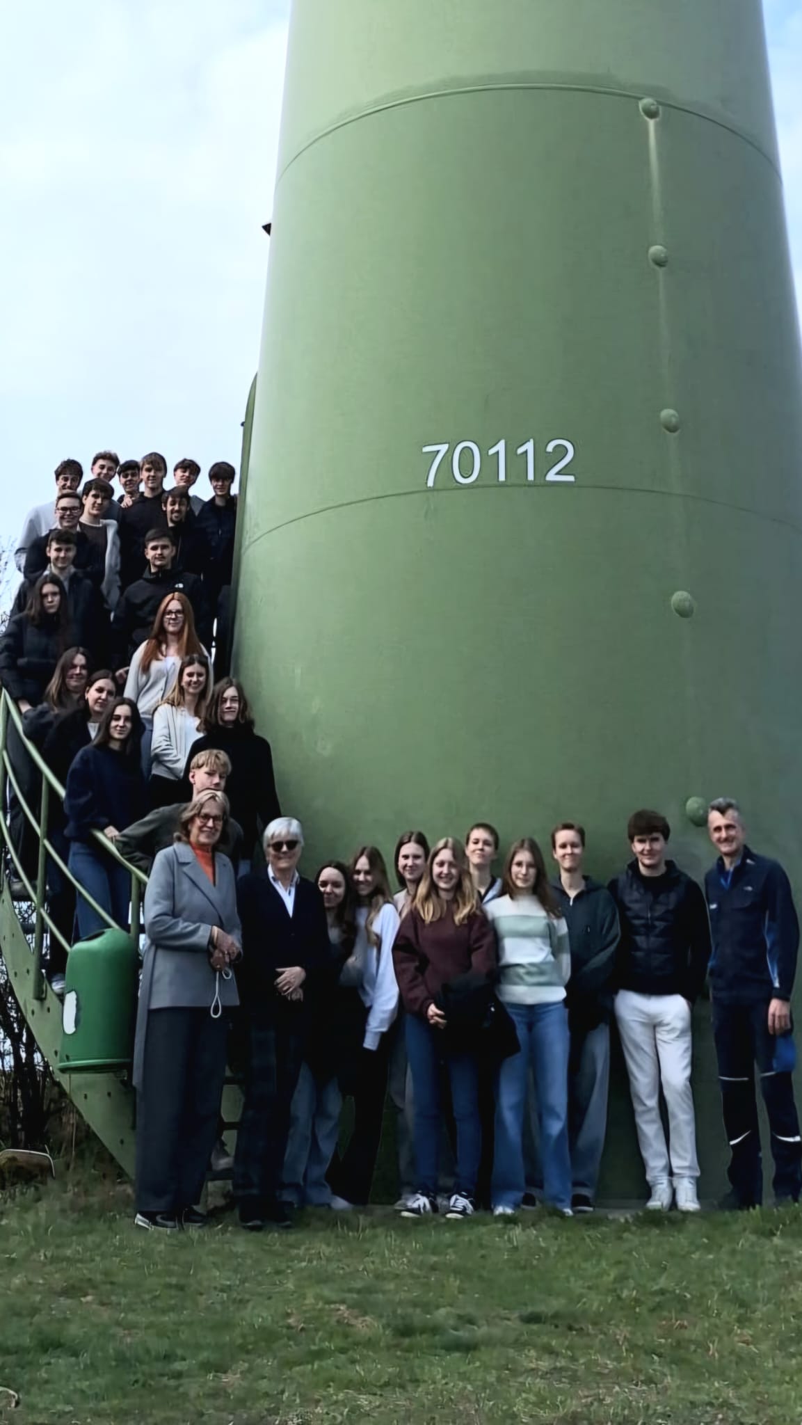 Eine Gruppe von Menschen steht für ein Foto vor einem großen grünen Turm mit der Nummer „70112“, einige auf einer Treppe, andere davor auf einer Wiese.