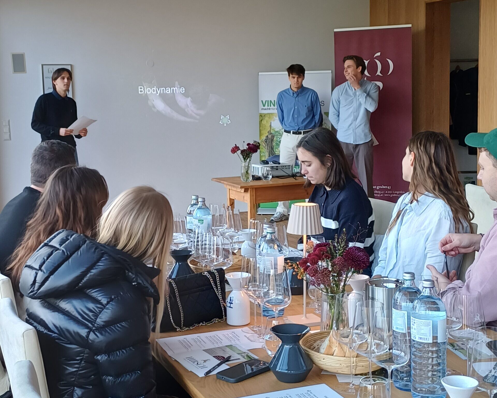 Drei Schüler halten Vortrag über Biodynamie. Gäste sitzen zuhörend an einem Tisch.