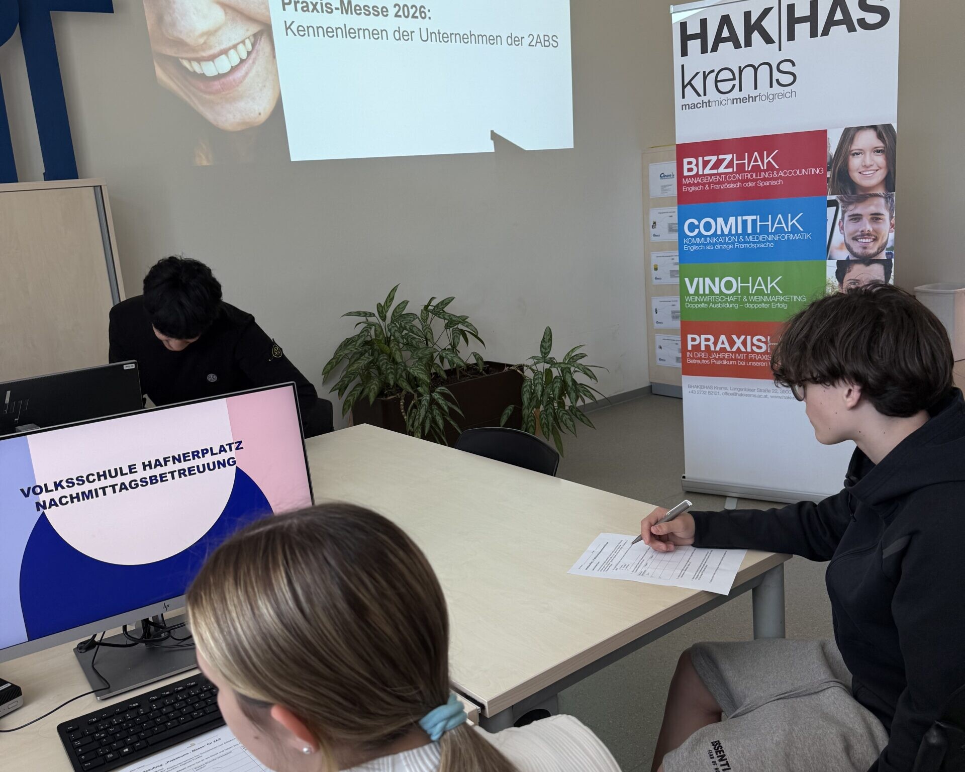 Schüler:innen arbeiten rund um einen Tisch, an die Wand ein Bild mit der Aufschrift