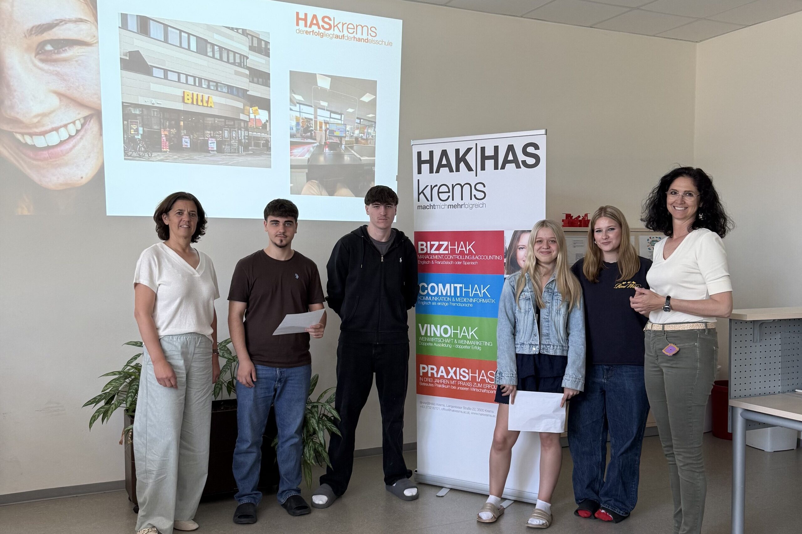 2 Lehrerinnen, 2 Schüler und 2 Schülerinnen lächeln in die Kamera, zwischen ihnen ein Banner der HAK|HASkrems.