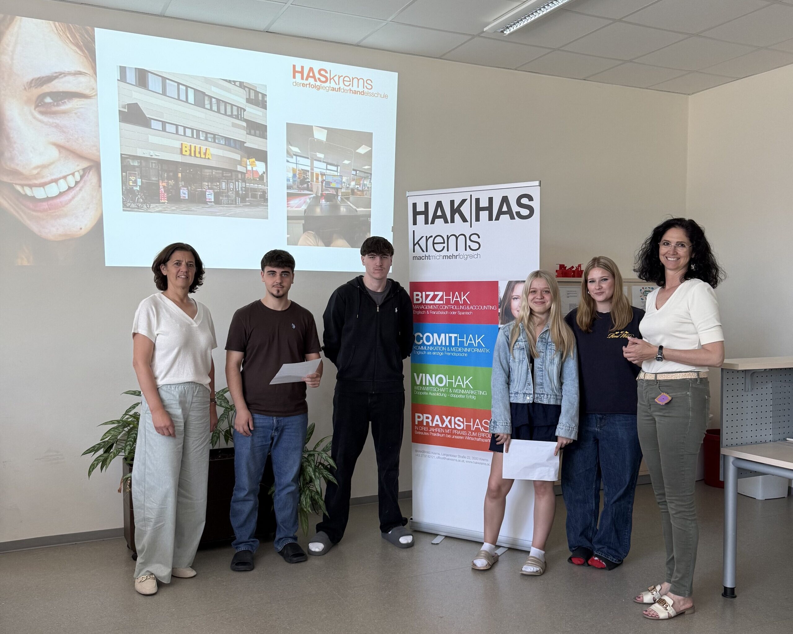 2 Lehrerinnen, 2 Schüler und 2 Schülerinnen lächeln in die Kamera, zwischen ihnen ein Banner der HAK|HASkrems.