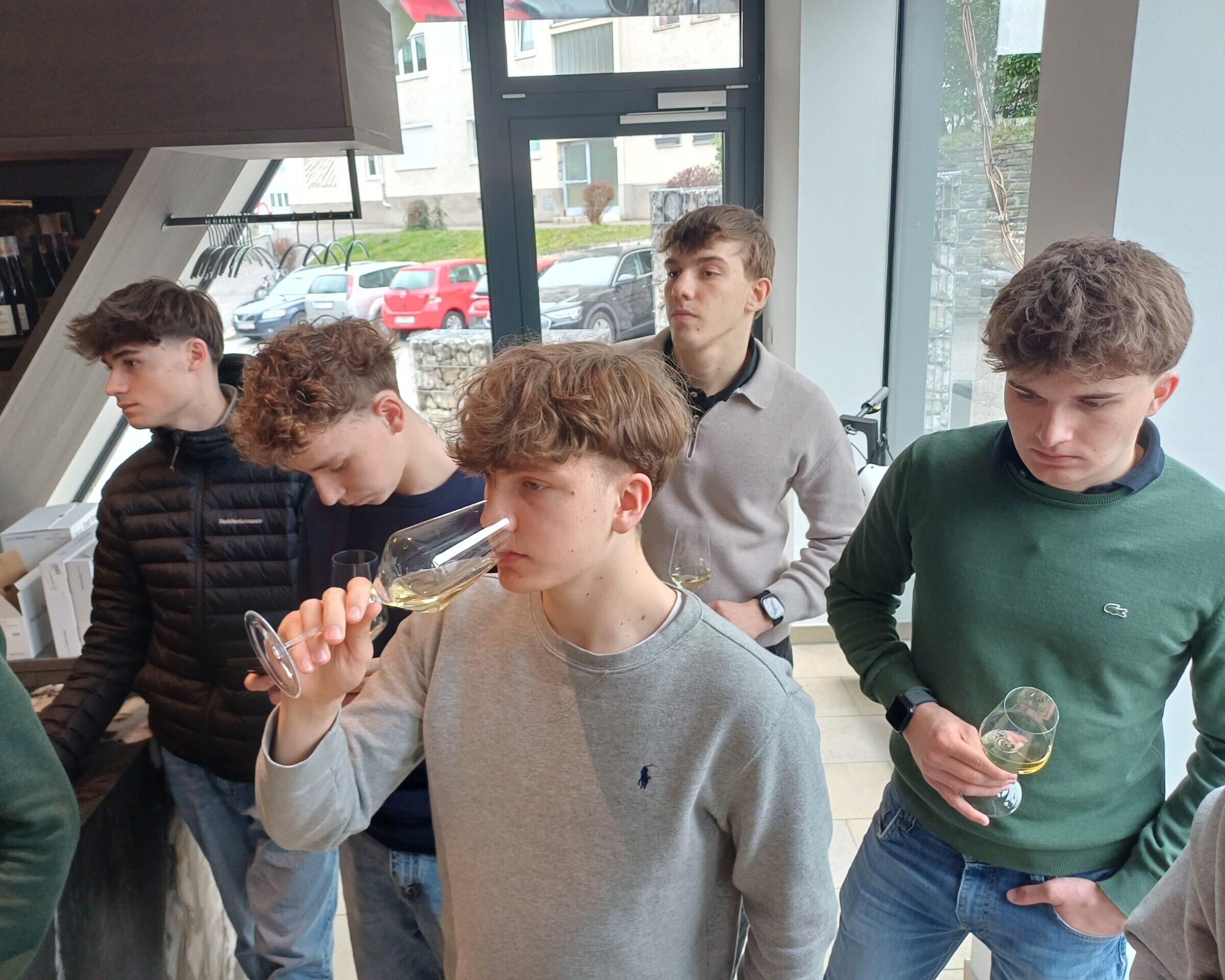 5 Schüler mit einem Weinglas in der Hand und ein Schüler riecht von seinem Wein gefüllten Weinglas.