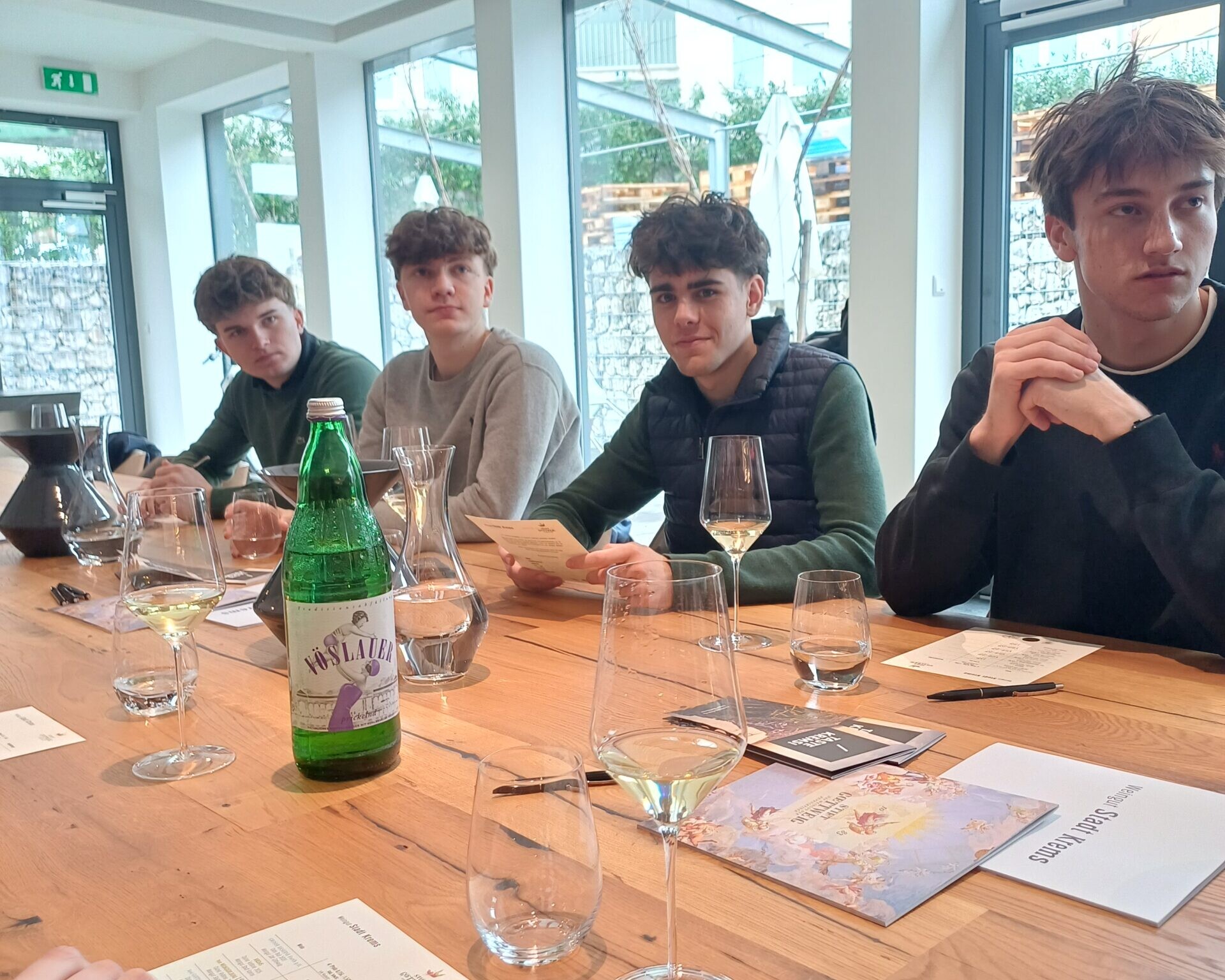 4 Schüler an einem Tisch sitzend mit Weingläser und Karten vor ihnen.