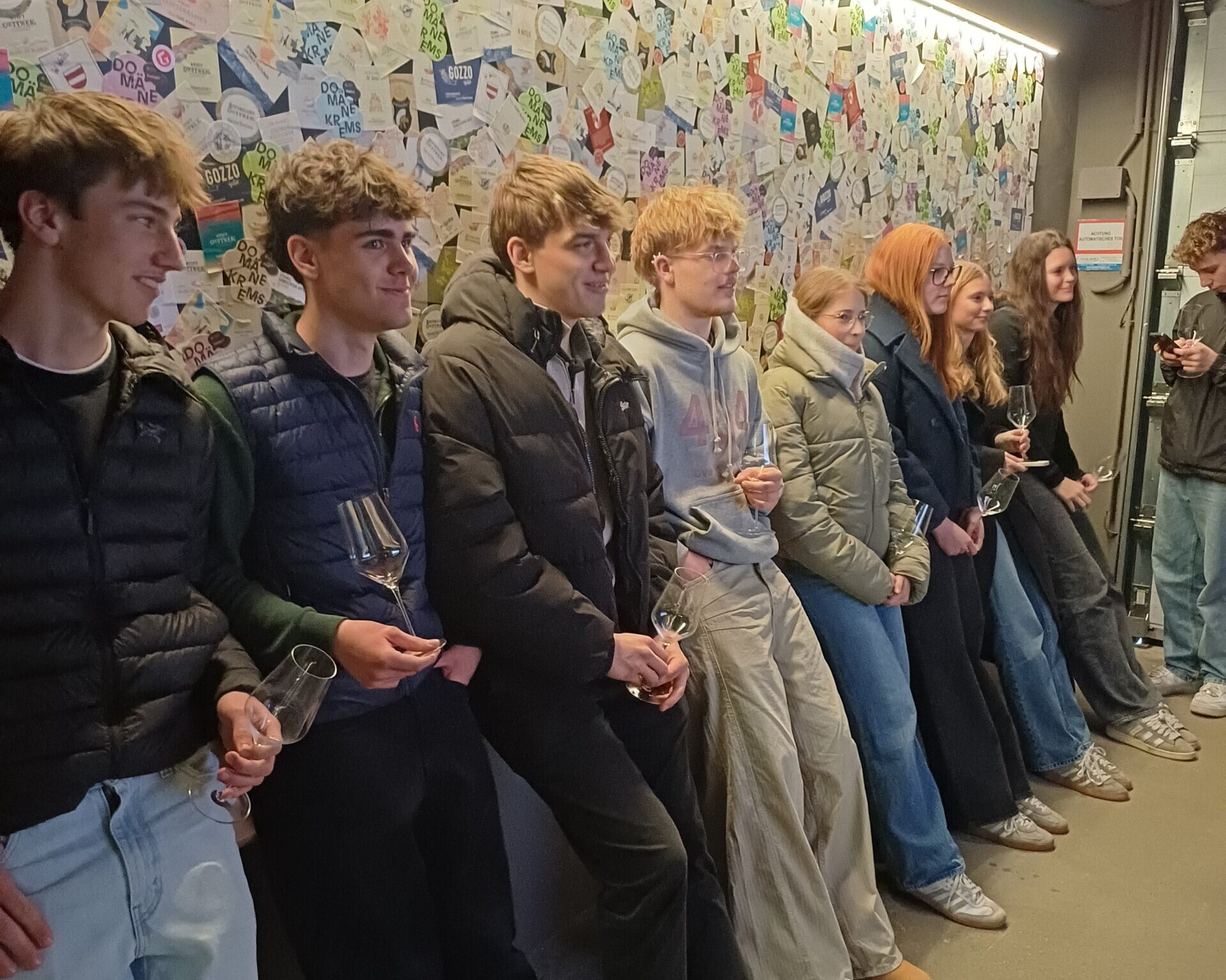 8 Schüler:innen stehen mit einem Weingals in der Hand an einer Wand.