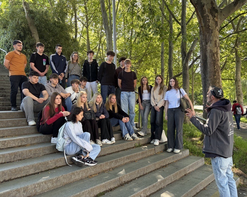 Eine Gruppe Jugendlicher sitzt auf Treppen im Park und hört einem Guide aufmerksam zu.