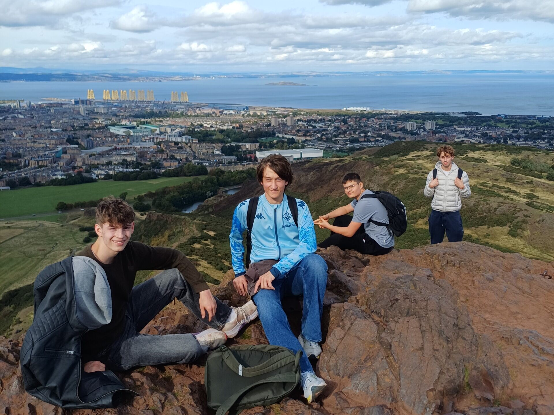 Vier junge Männer sitzen auf einem Felsen mit Blick auf Edinburgh und das Meer.