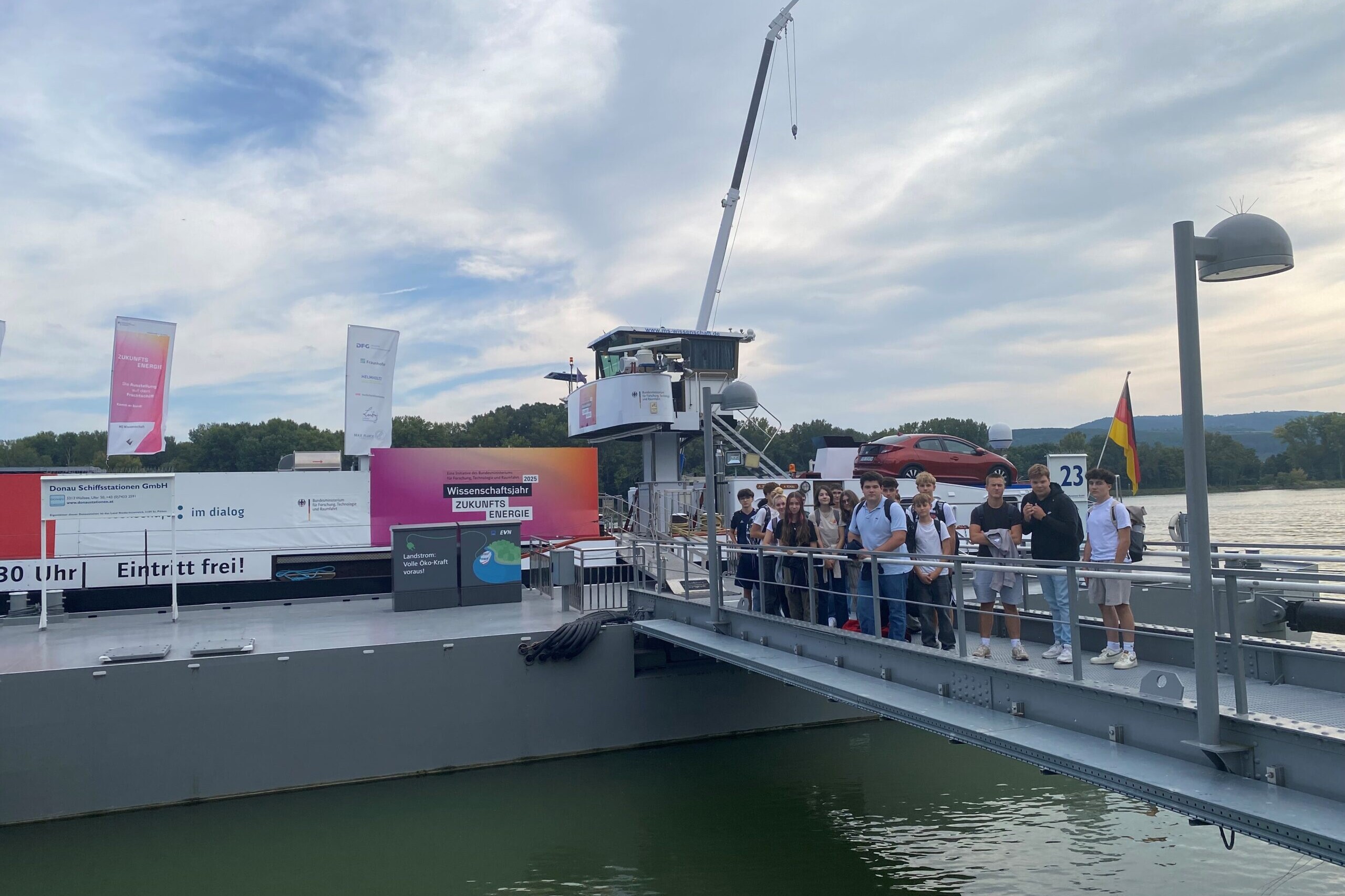 15 Schülerinnen und Schüler blicken direkt in die Kamera und stehen auf dem Steg vor dem Schiff der MS Wissenschaft