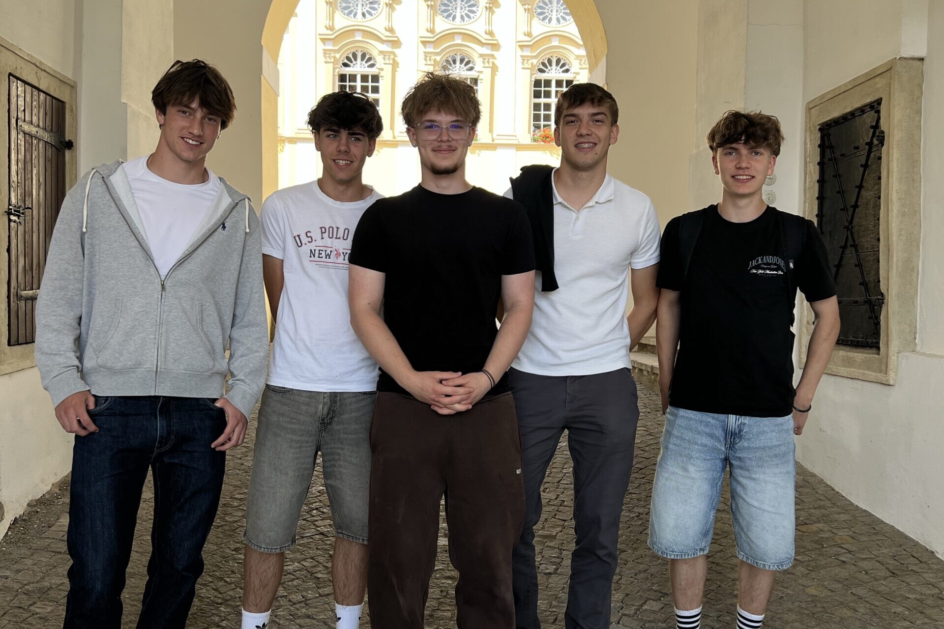 Fünf Schüler stehen für ein Gruppenfoto in einem historischen Torbogen mit Blick auf einen Innenhof.