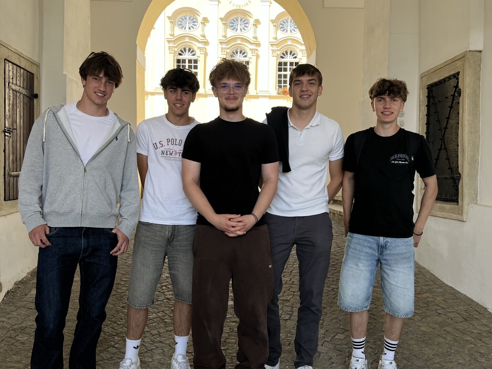 Fünf Schüler stehen für ein Gruppenfoto in einem historischen Torbogen mit Blick auf einen Innenhof.