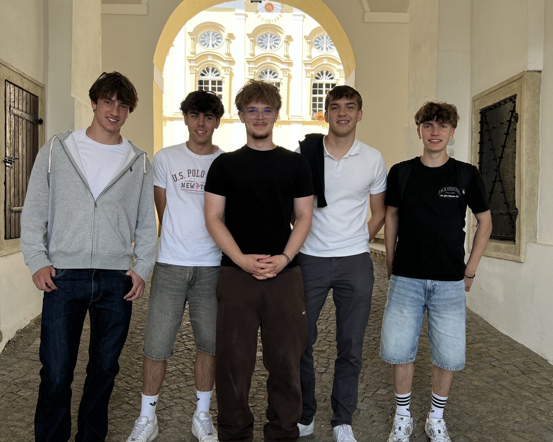 Fünf Schüler stehen für ein Gruppenfoto in einem historischen Torbogen mit Blick auf einen Innenhof.
