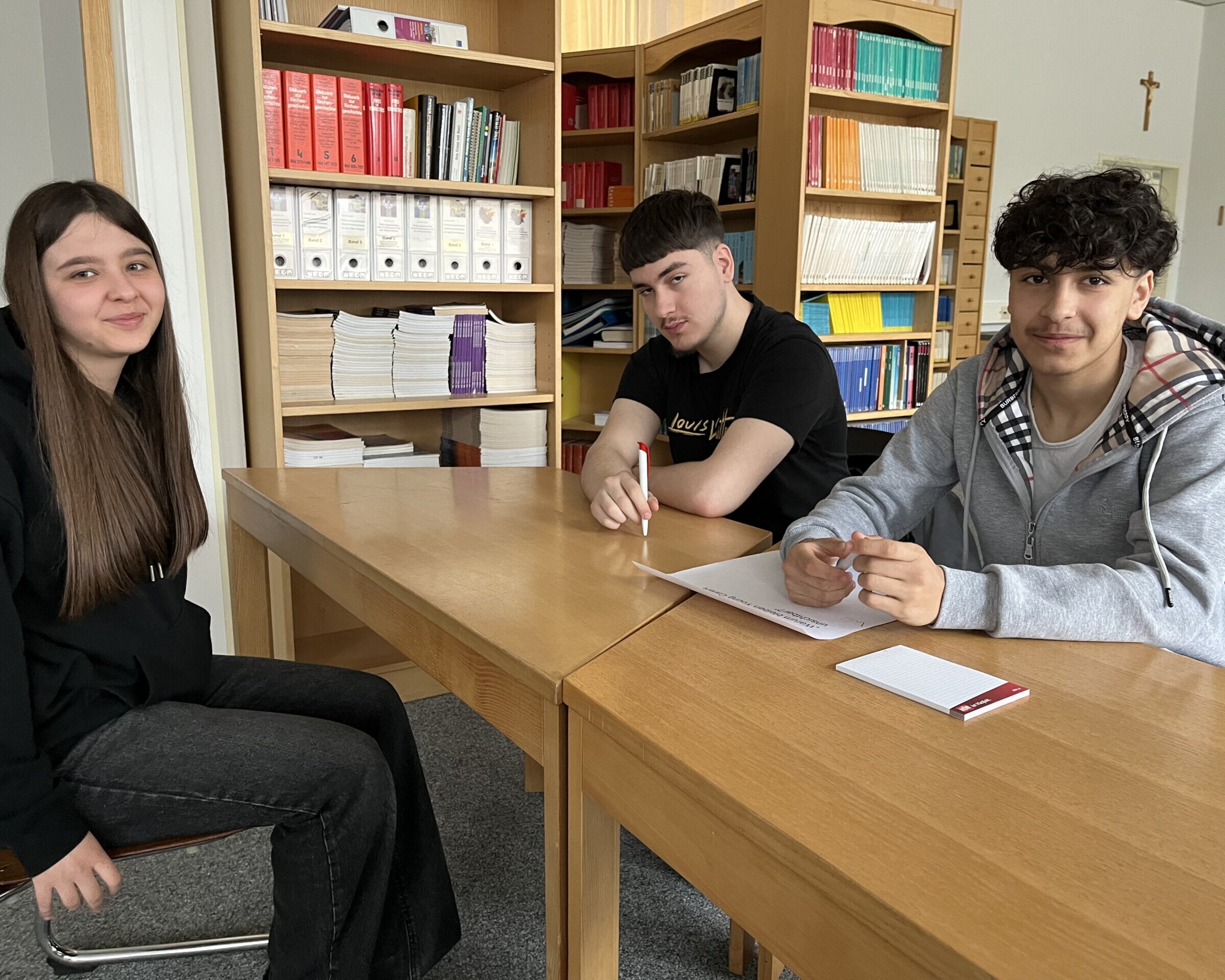 2 Schüler und 1 Schülerin sitzen rund um einen Tisch und vor ihnen sind Zettel.