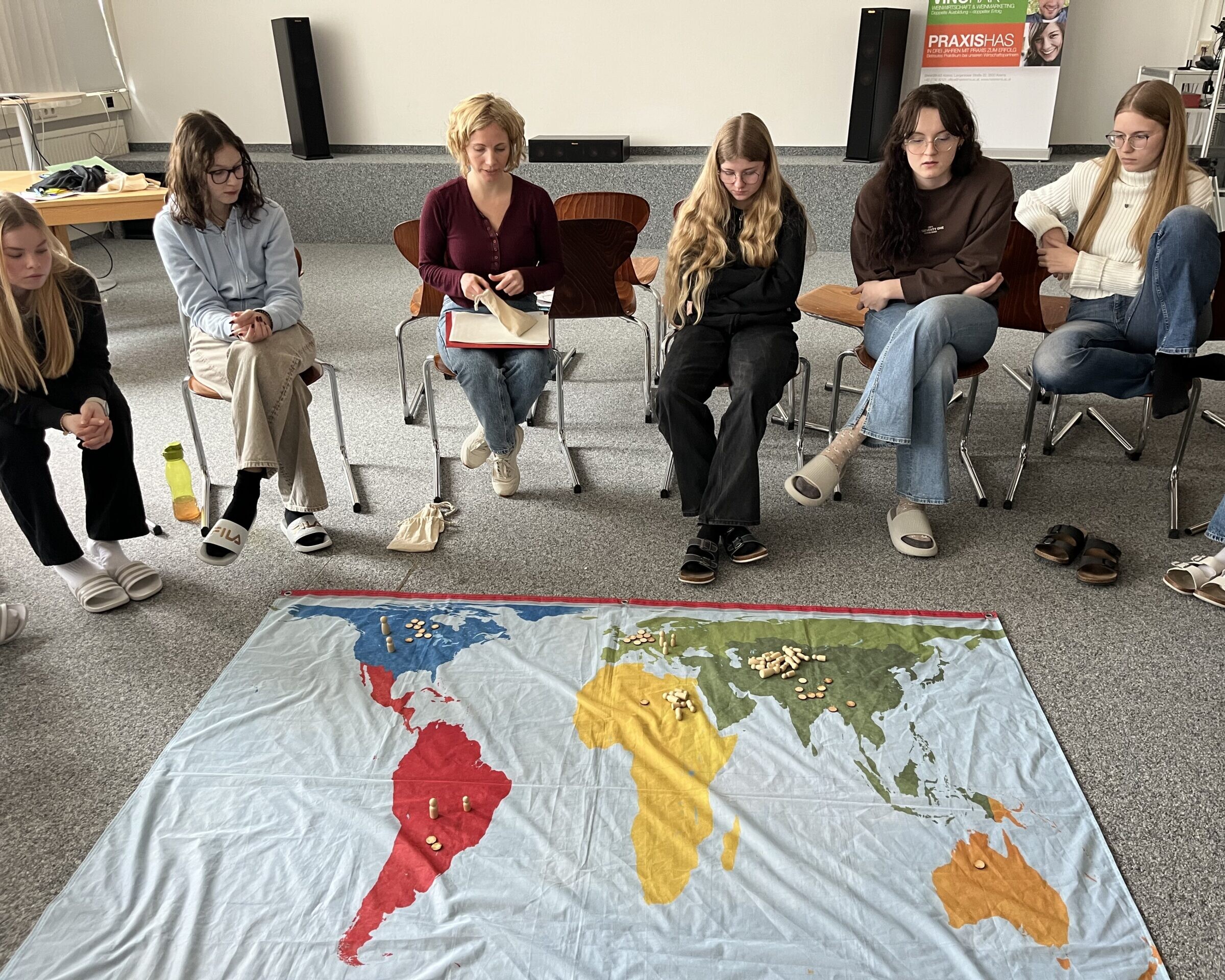 5 Schülerinnen und 1 Betreuerin sitzen hinter einer Weltkarte und blicken darauf.