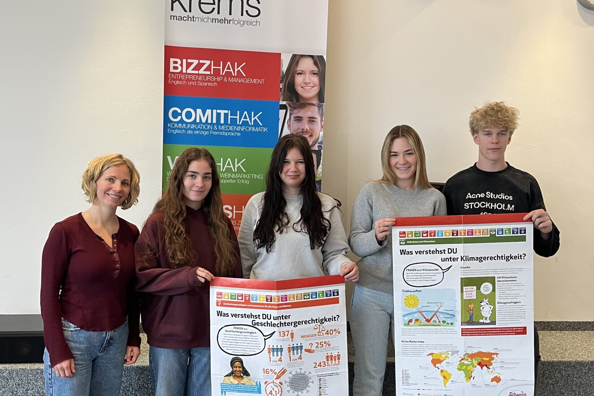 1 Betreuerin, 3 Schülerinnen und 1 Schüler lächeln in die Kamera, die Schüler:innen halten 2 NGO's Plakate.