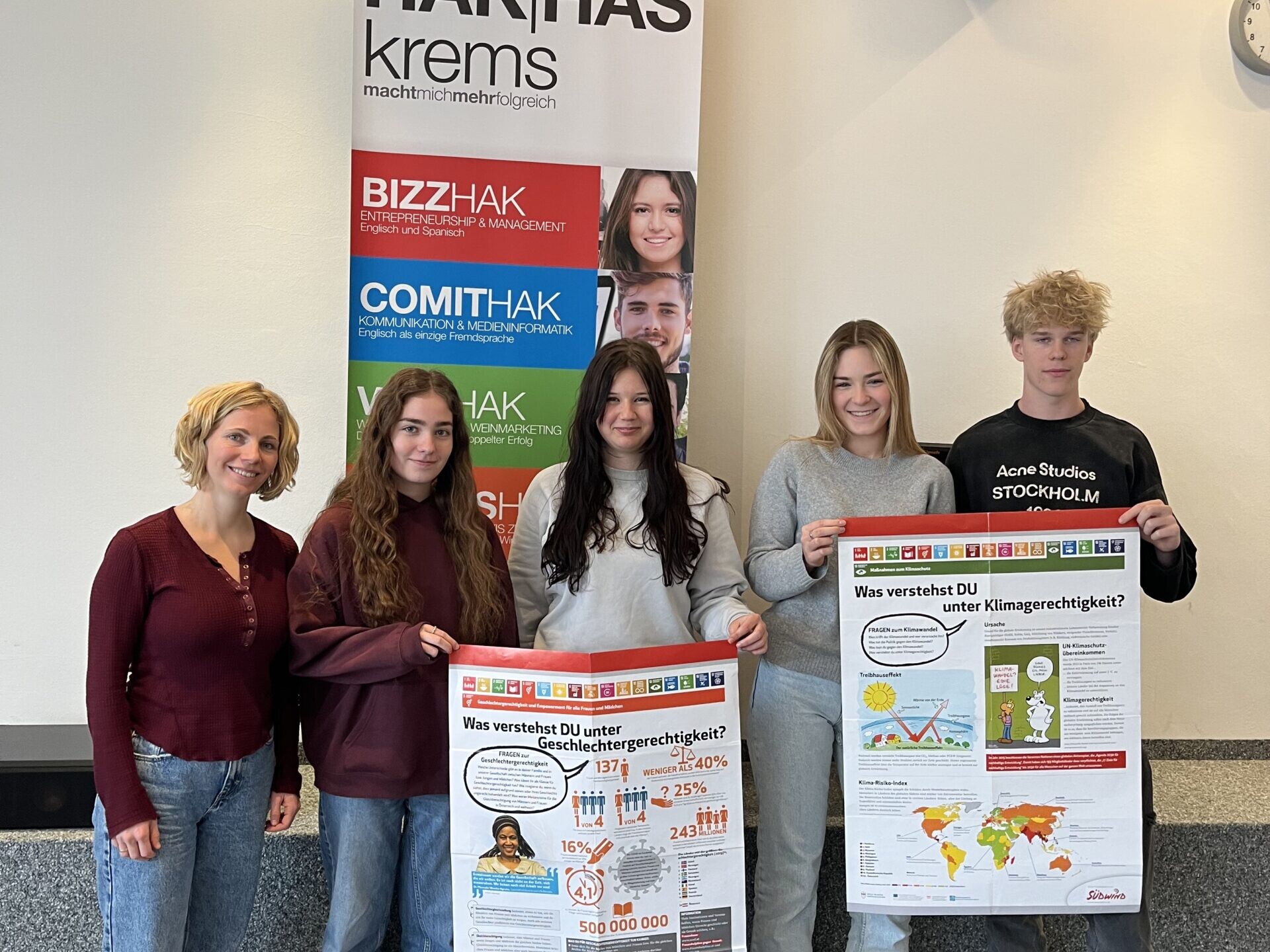 1 Betreuerin, 3 Schülerinnen und 1 Schüler lächeln in die Kamera, die Schüler:innen halten 2 NGO's Plakate.