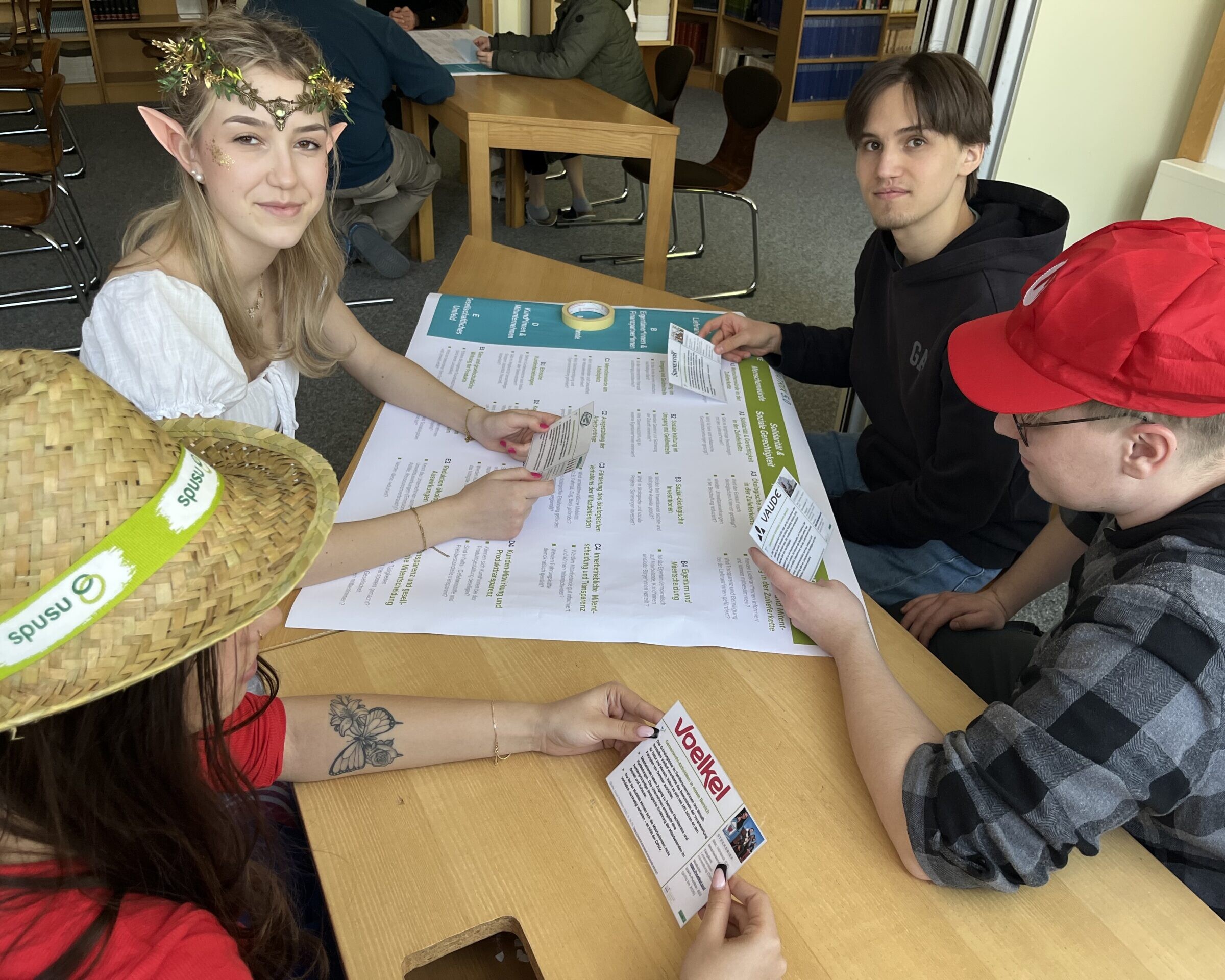 Schüler:innen arbeiten rund um einen Tisch, darauf liegend ein Plakat.