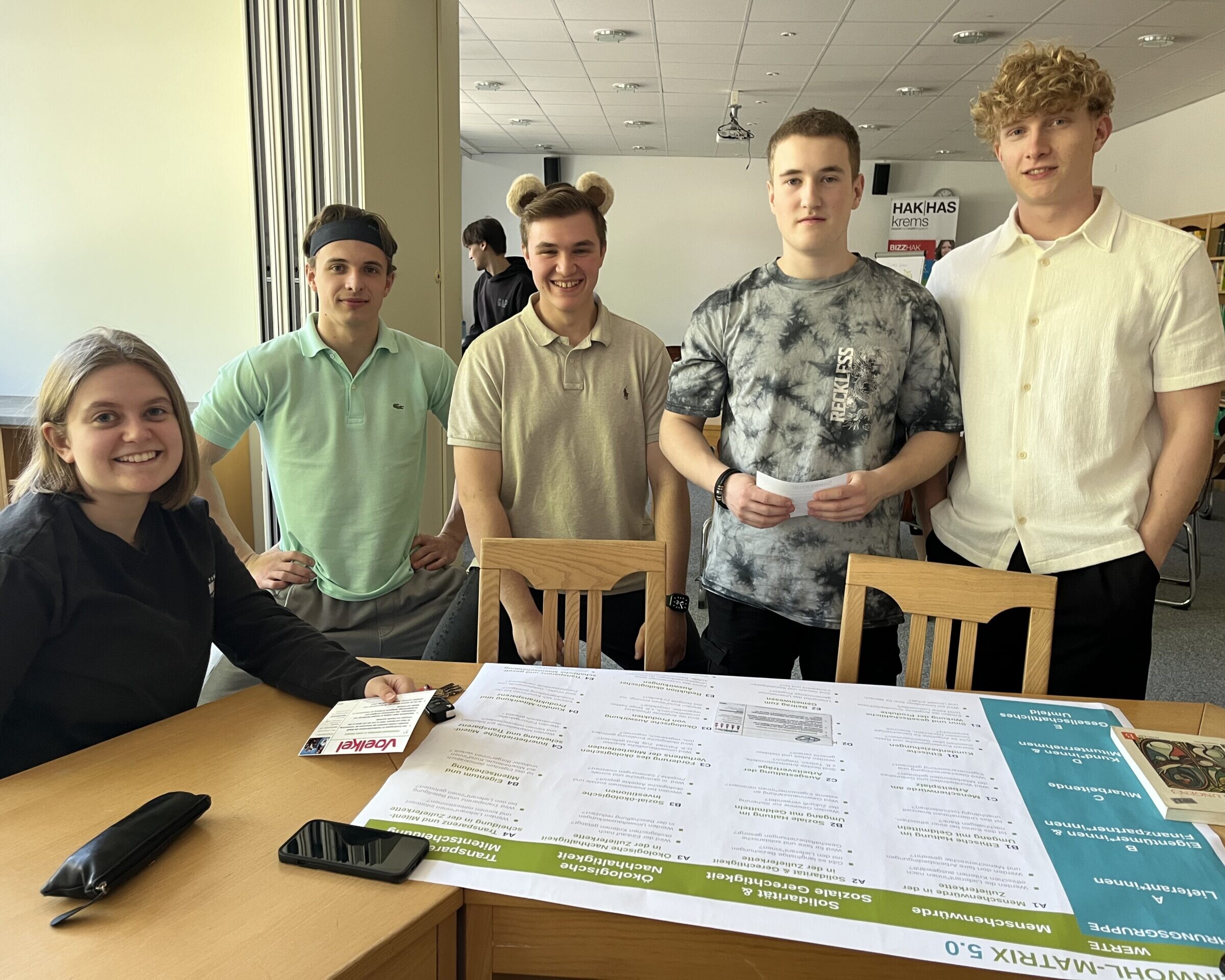 Schüler:innen arbeiten rund um einen Tisch, darauf liegend ein Plakat.