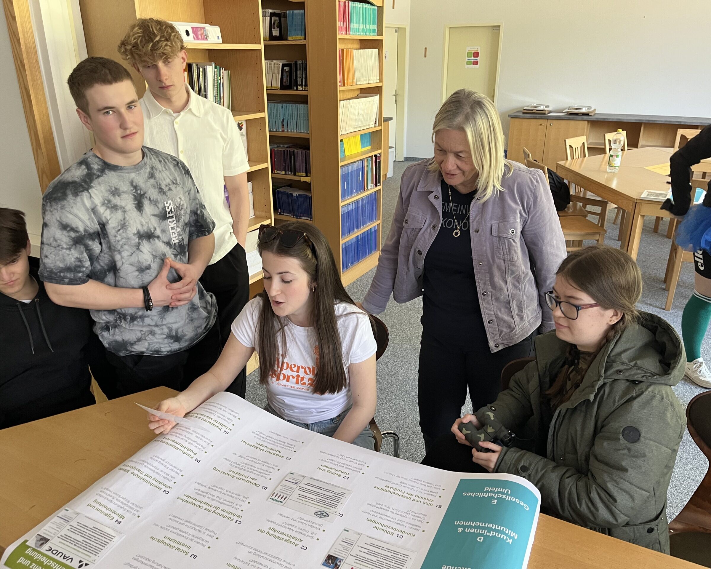 Schüler:innen arbeiten rund um einen Tisch, darauf liegend ein Plakat.