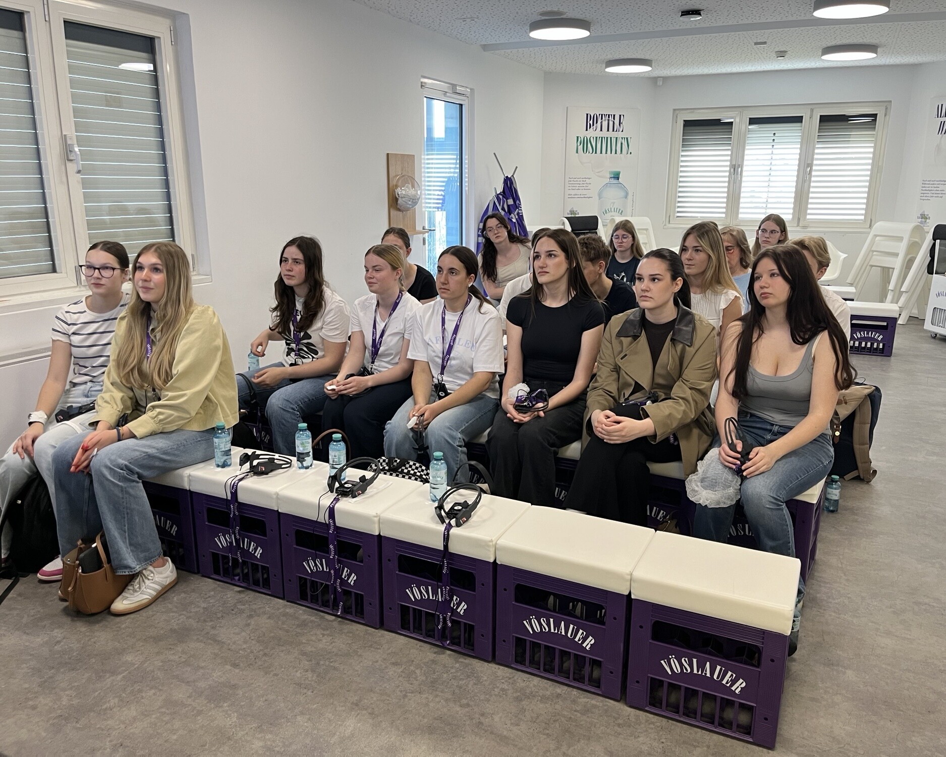 2 Lehrerinnen und eine Gruppe Schüler: innen sitzt bei einer Präsentation in einem modernen Seminarraum.