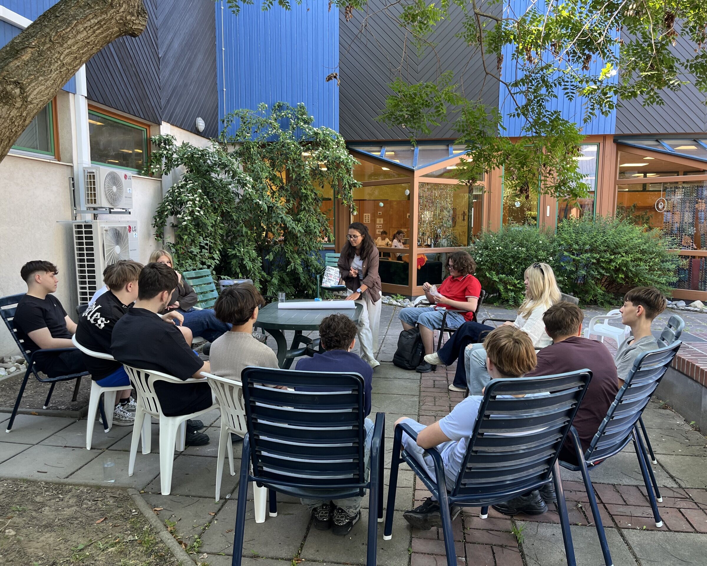 Sitzkreis um einen Tisch mit Schüler*innen und Betreuungsperson.