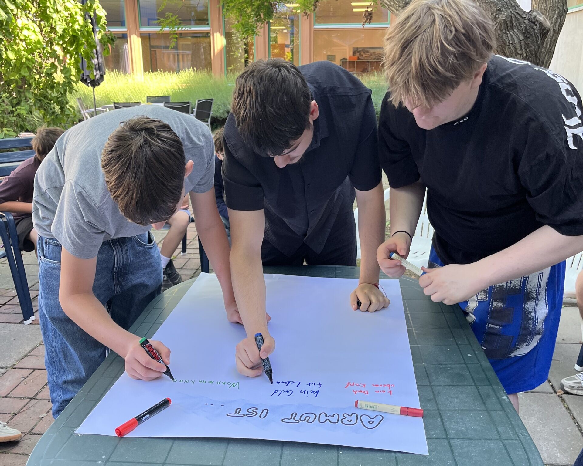 3 Schüler schreiben auf Tisch liegendem Plakat.