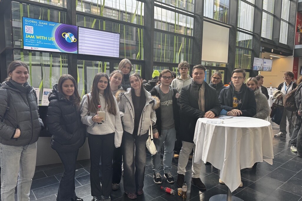 Eine Gruppe junger Schüler*innen stehen lächelnd in einer hellen Eingangshalle und posiert gemeinsam für ein Foto.