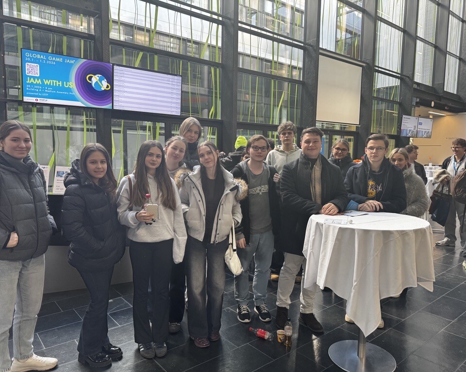 Eine Gruppe junger Schüler*innen stehen lächelnd in einer hellen Eingangshalle und posiert gemeinsam für ein Foto.