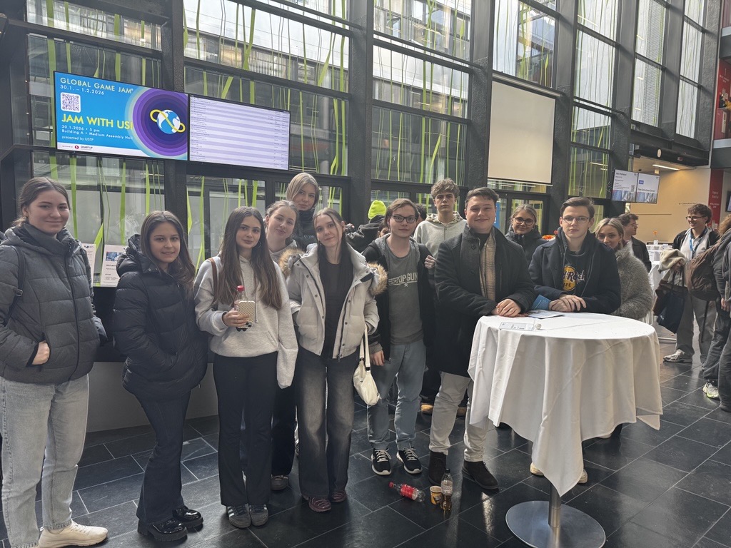 Eine Gruppe junger Schüler*innen stehen lächelnd in einer hellen Eingangshalle und posiert gemeinsam für ein Foto.