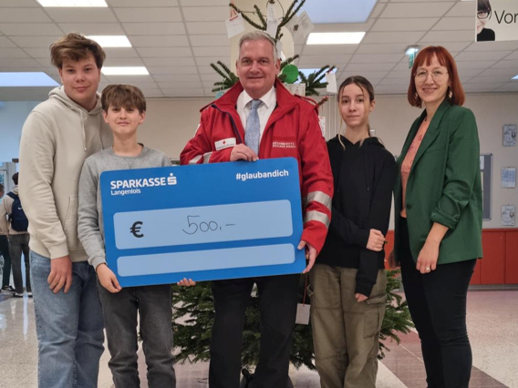 Lehrer und Lehrerin mit drei Schüler*innen und € 500 Spendentafel, direkt in die Kamera blickend.