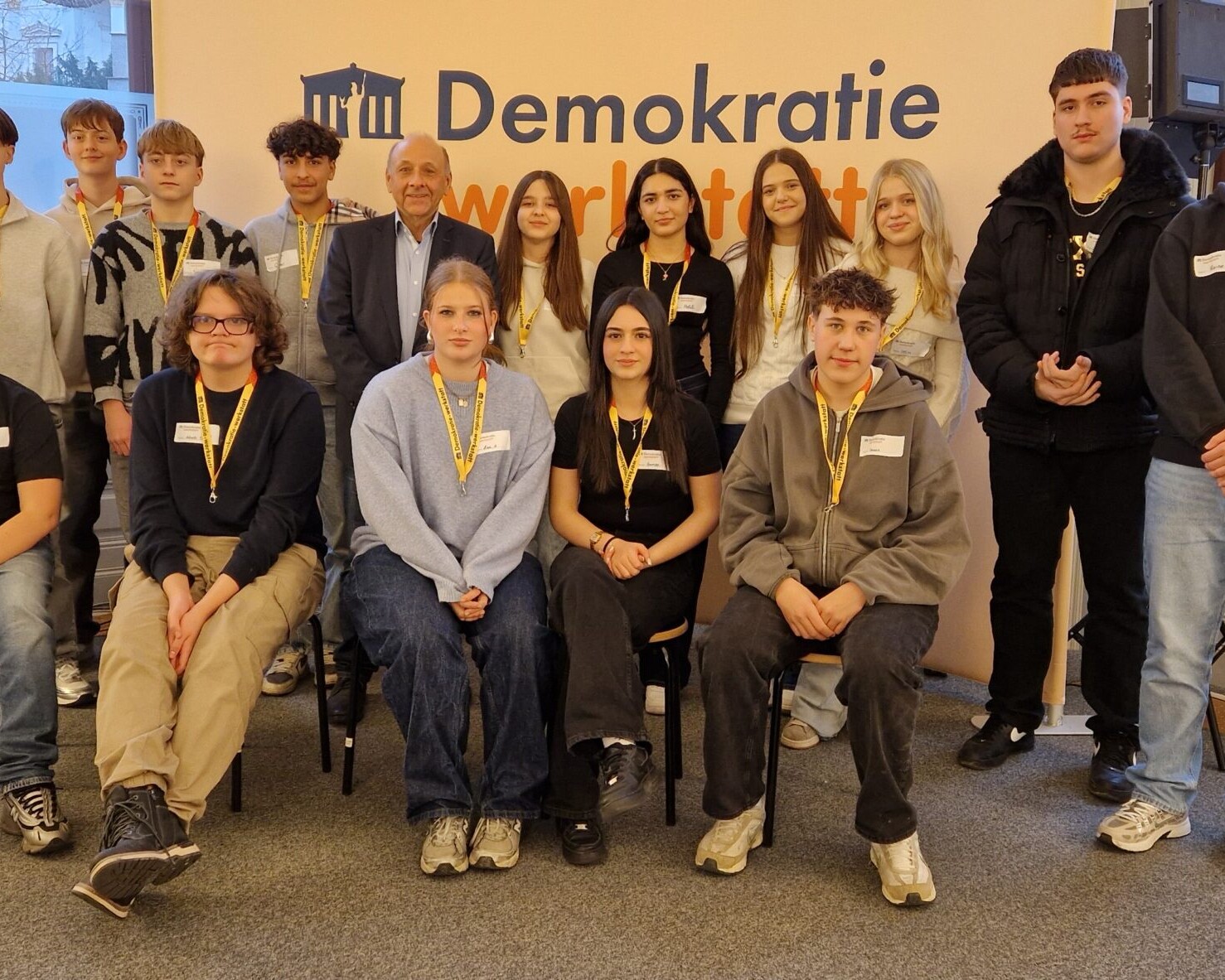 15 Schüler*innen mit ORF-Journalisten Dr. Robert Stoppacher bei der Demokratiewerkstatt, direkt in die Kamera blickend.