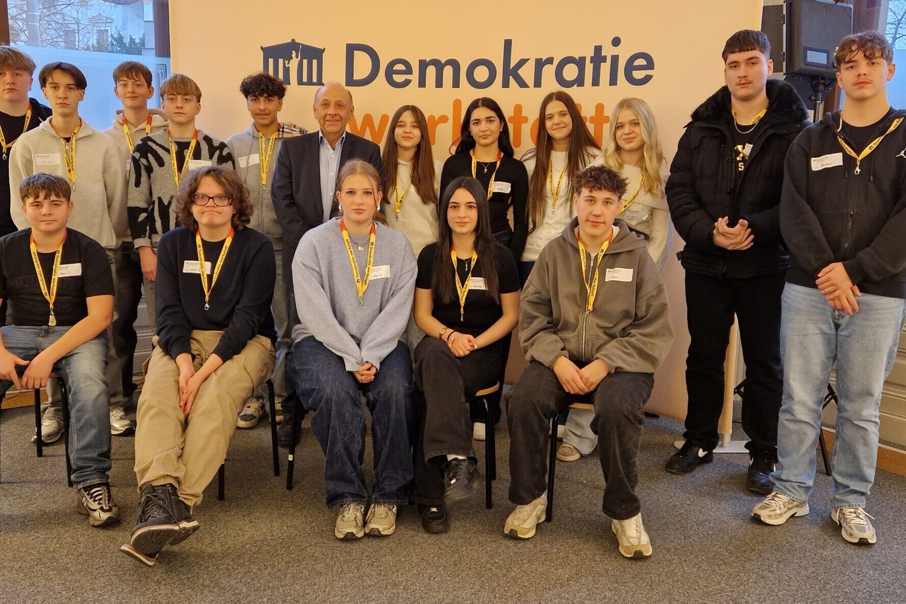 15 Schüler*innen mit ORF-Journalisten Dr. Robert Stoppacher bei der Demokratiewerkstatt, direkt in die Kamera blickend.