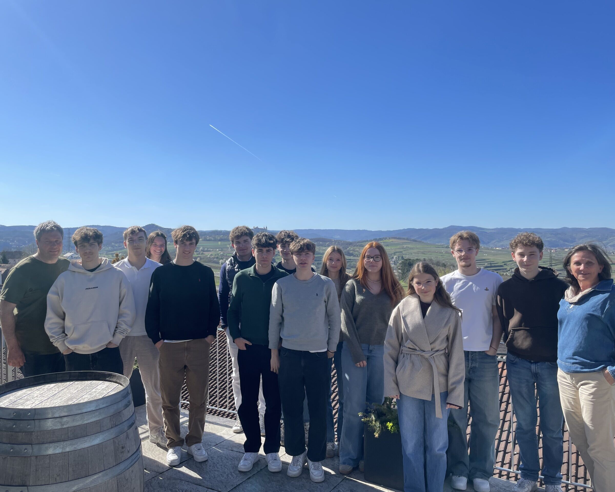 Gruppe von Schülerinnen und Schüler steht auf einer Terrasse mit Blick über Weinberge unter blauem Himmel