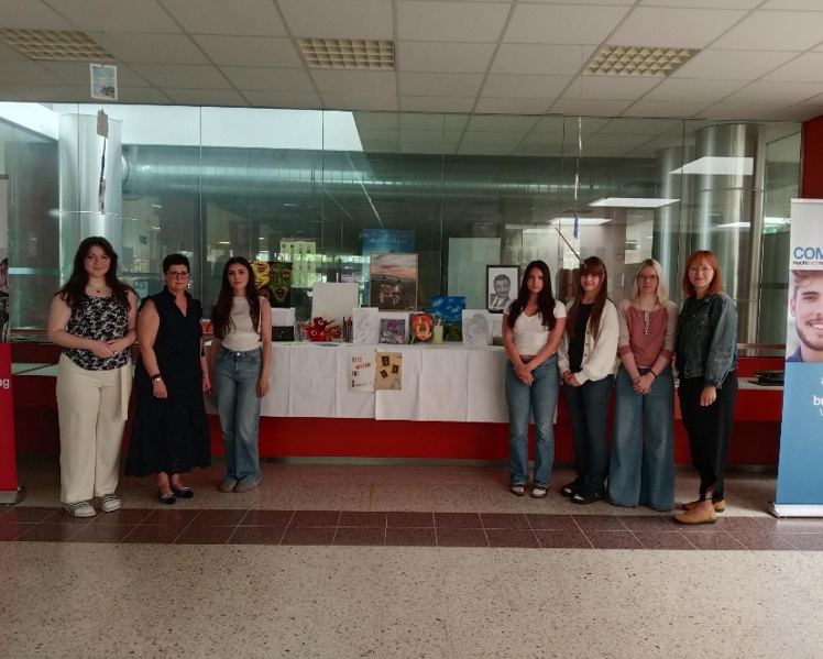 Fünf Schülerinnen präsentieren gemeinsam mit einer Lehrerin und einer Direktorin eine Ausstellung mit Kunstwerken und Projekten in einem Schulgebäude.