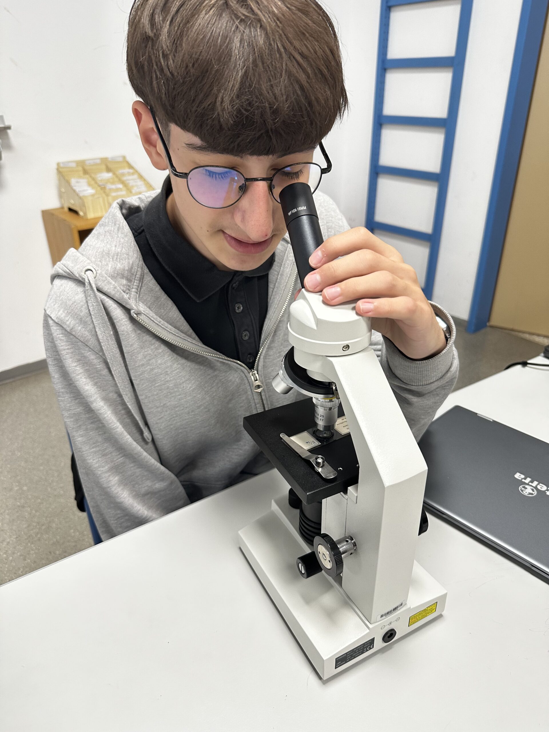 Schüler mit Brille blickt durch Mikroskop im Labor